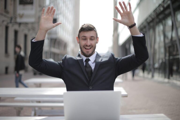 man in suite with hands up happy in front of laptop